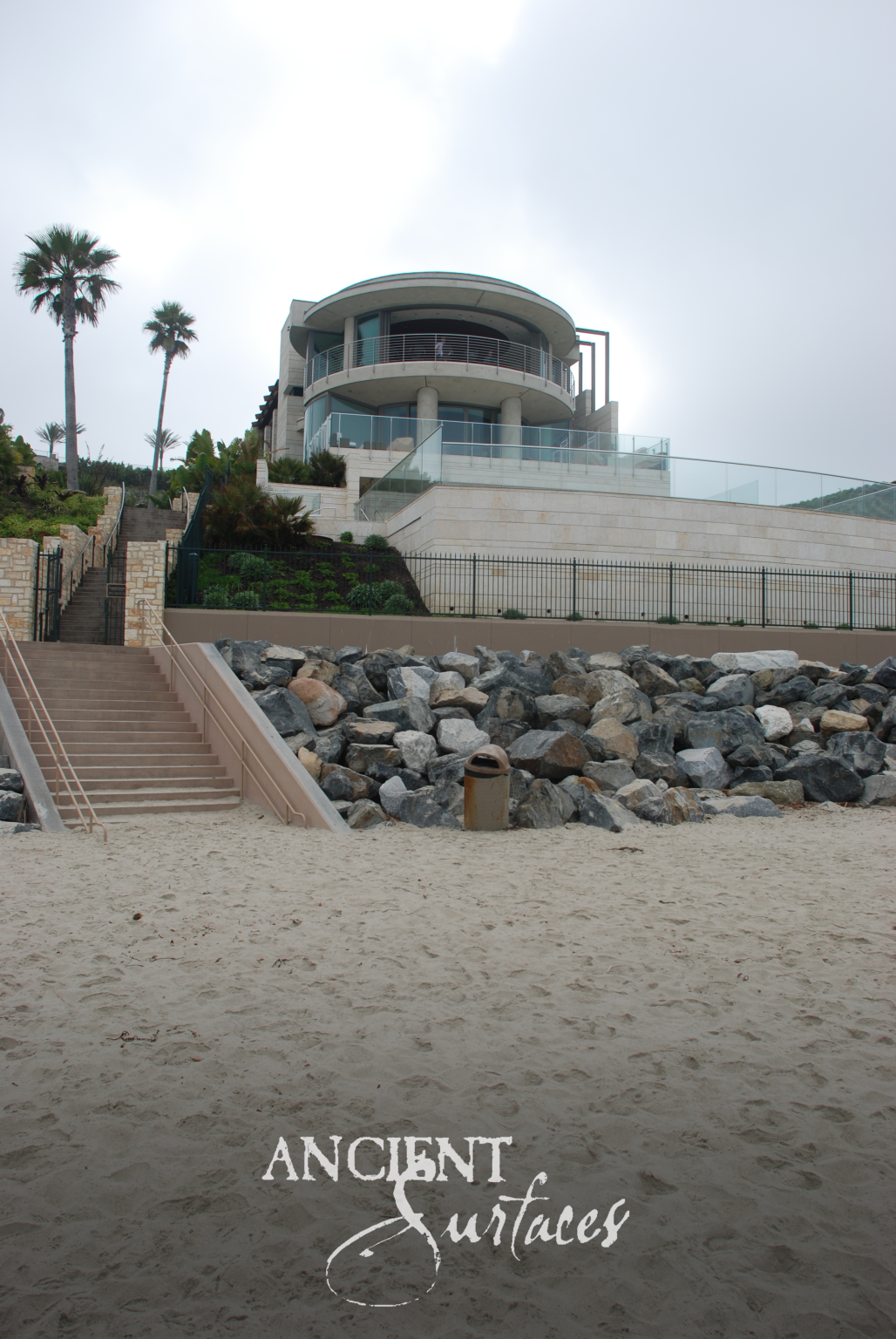 Limestone-clad oceanfront residence seen from the sand above a sea wall and stone stair