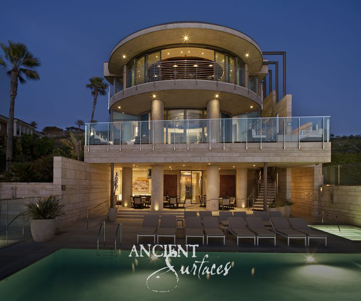Oceanfront residence clad in reclaimed limestone, lit at dusk above a pool terrace