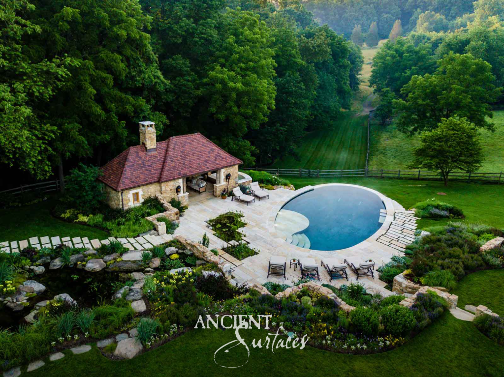 Aerial view of a stone pool house and antique limestone pool terrace set into a wooded estate