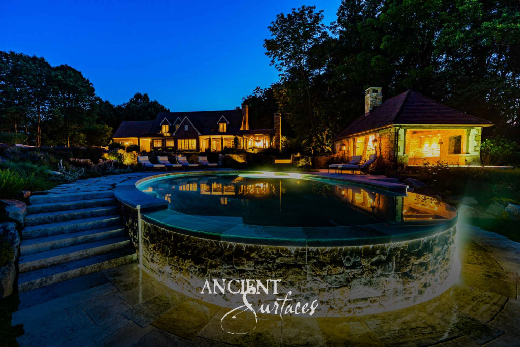 Reclaimed antique limestone pool coping, paving, and dry-stack stone walls at a country estate at blue hour