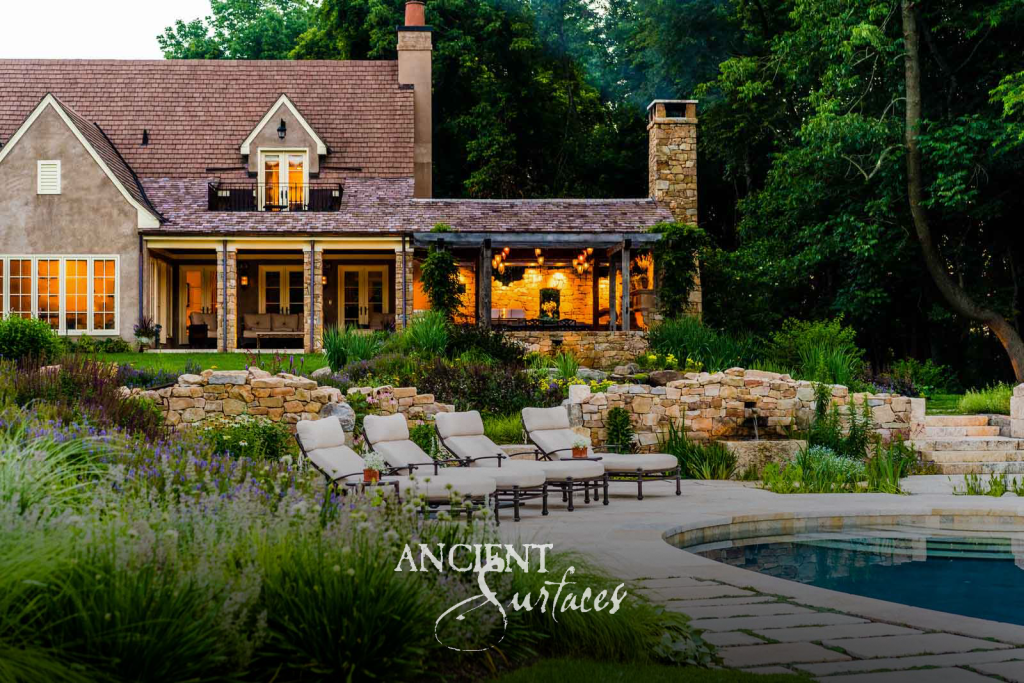 Estate garden at dusk with reclaimed limestone paving, dry-stack stone walls, and a lit stone loggia